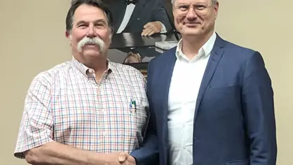 Skeeter LaDue shaking hands with Bo Larsen in front of a portrait of the first GEC CEO